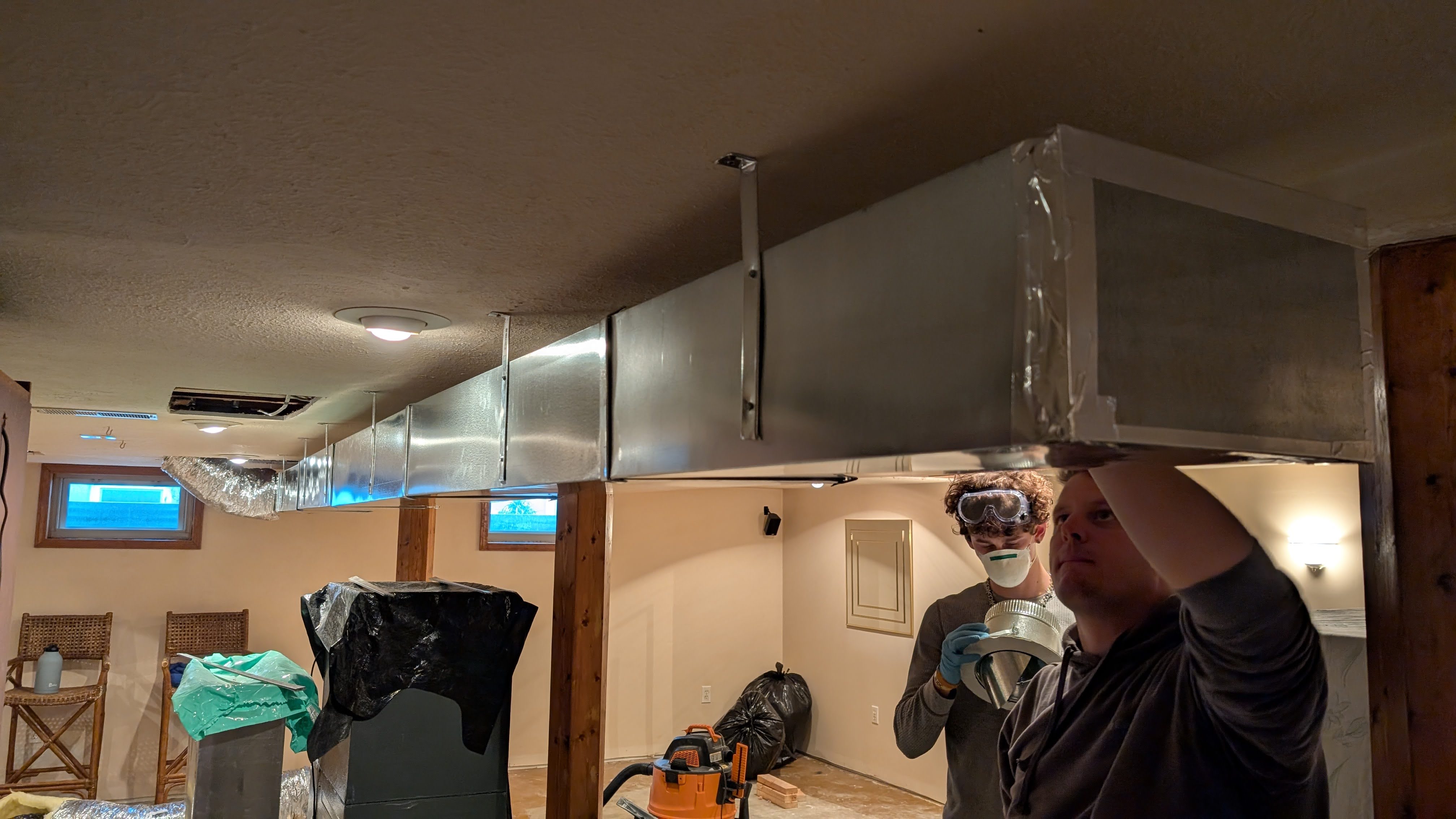 Two Henry Brothers technicians hanging sheet metal trunk ductwork in Jeffersonville Indiana basement