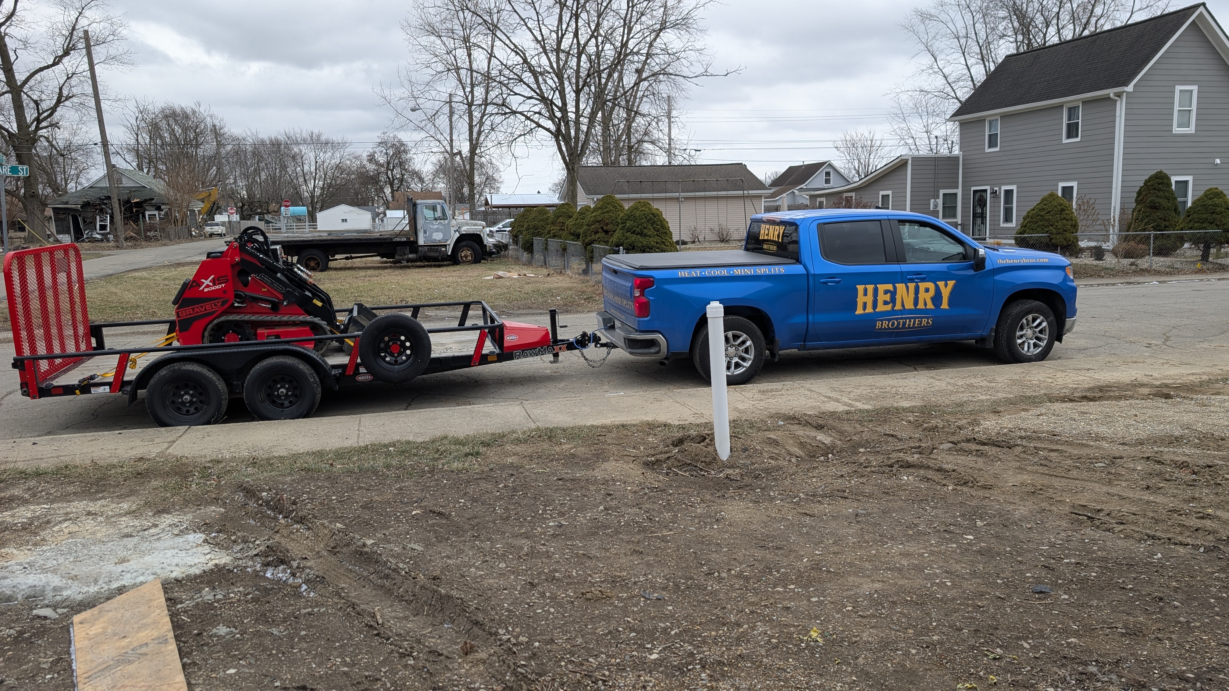 Henry Brothers branded blue Silverado truck and equipment trailer at mini-split install job site
