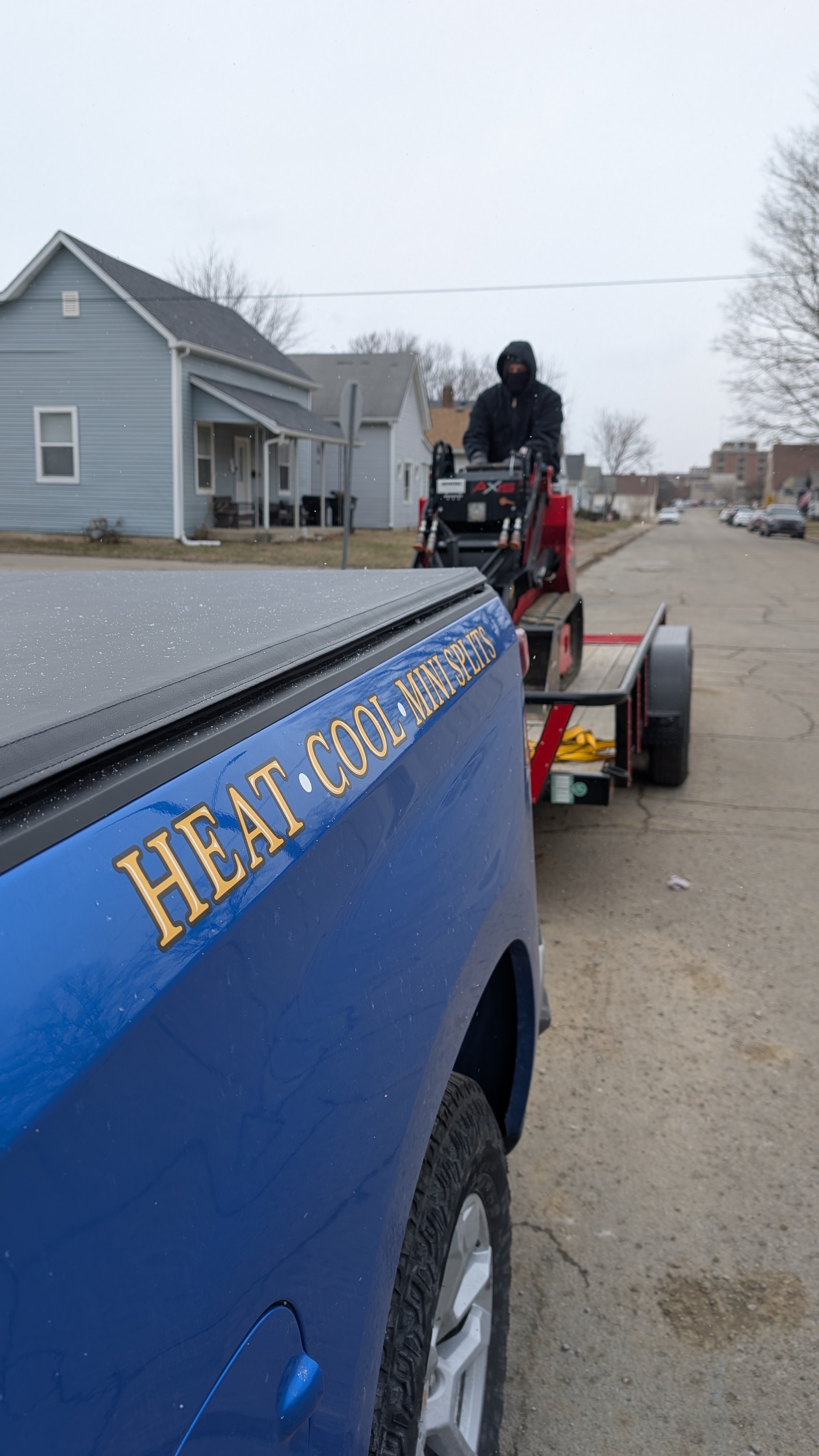Henry Brothers Heat Cool Mini Splits branded Silverado truck bed with technician on trailer in snowy neighborhood