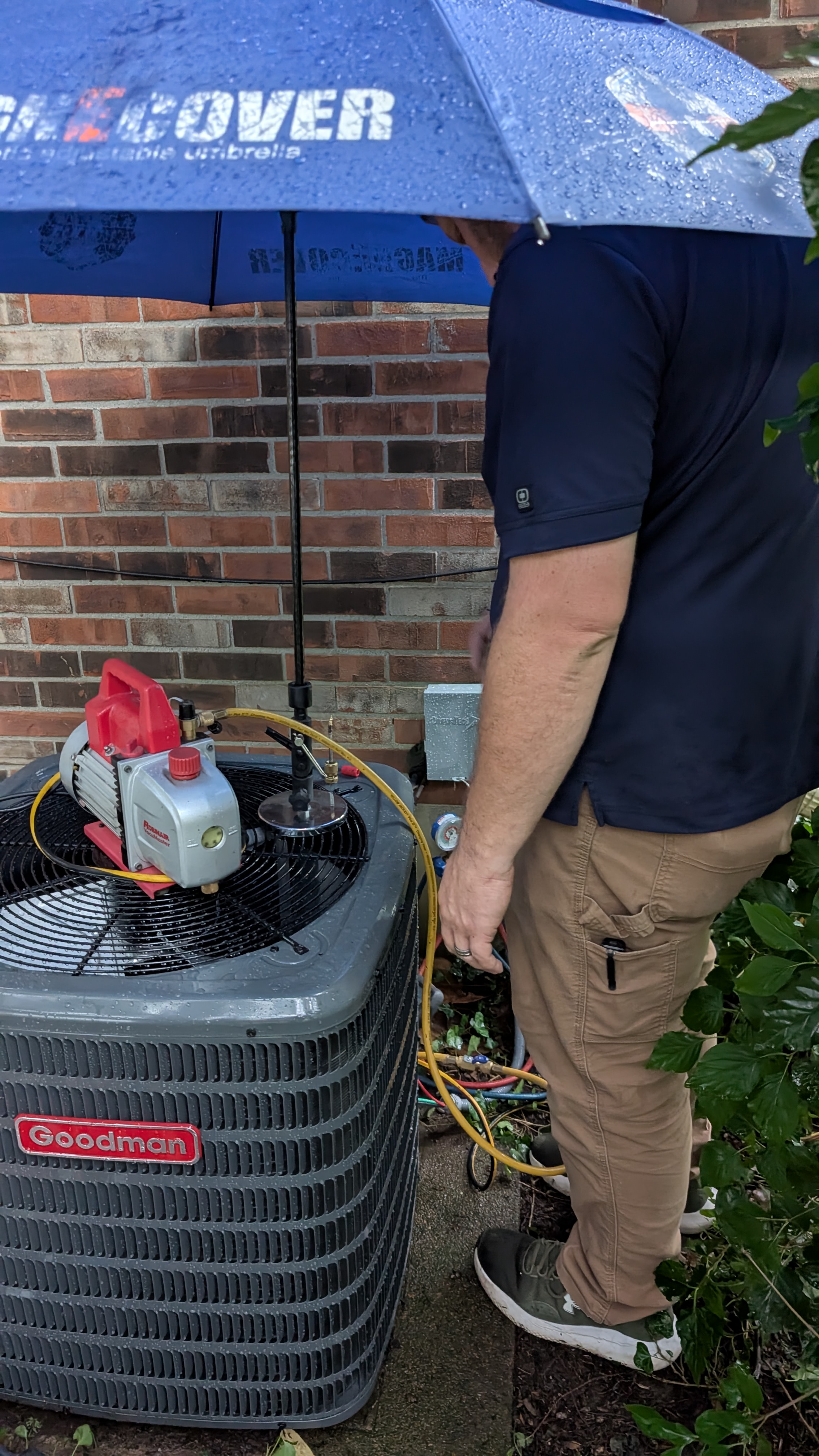 Henry Brothers technician vacuuming down Goodman AC condenser with manifold gauges in rain Jeffersonville Indiana