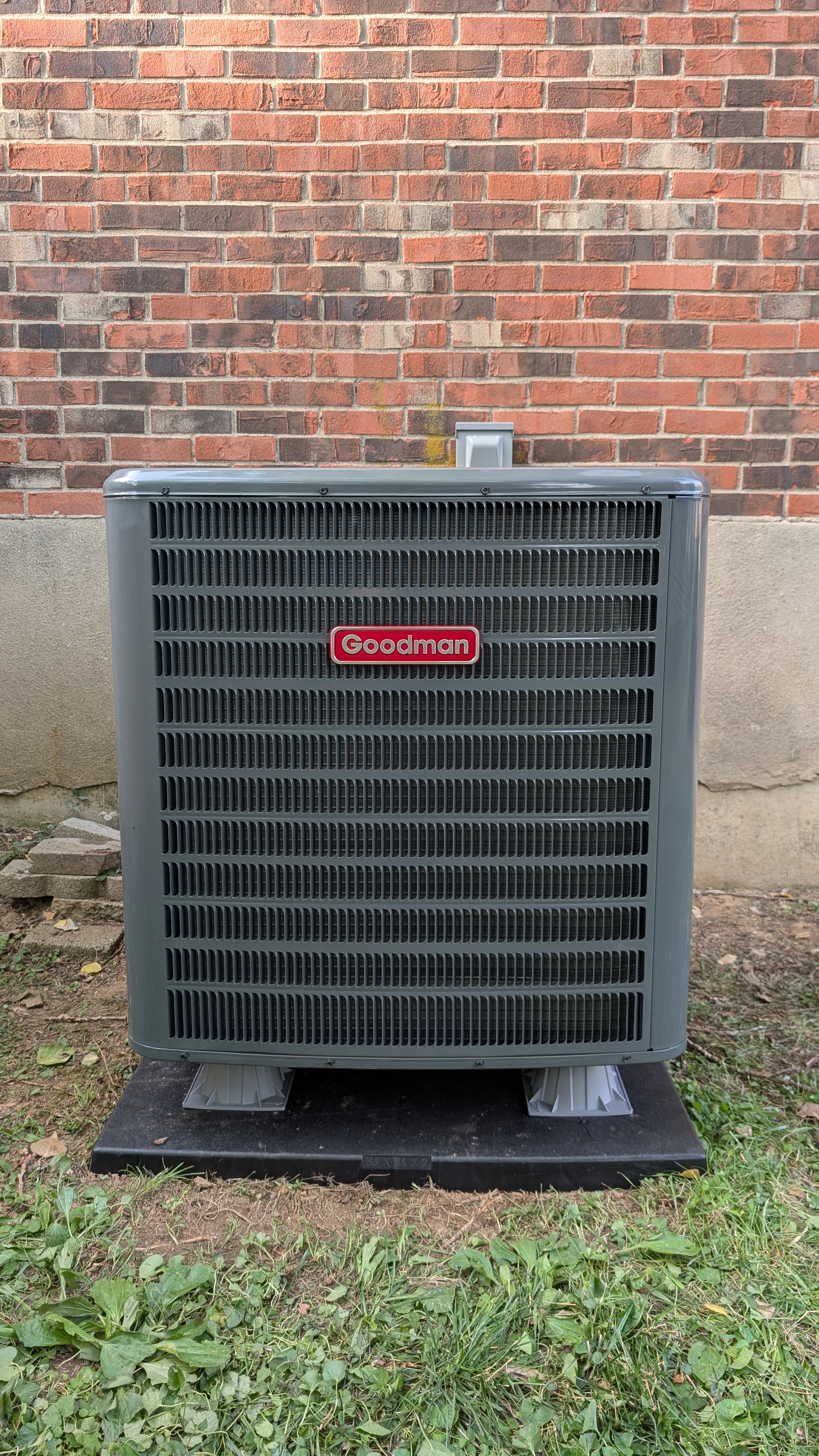 Goodman AC condenser front view against brick wall after HVAC service
