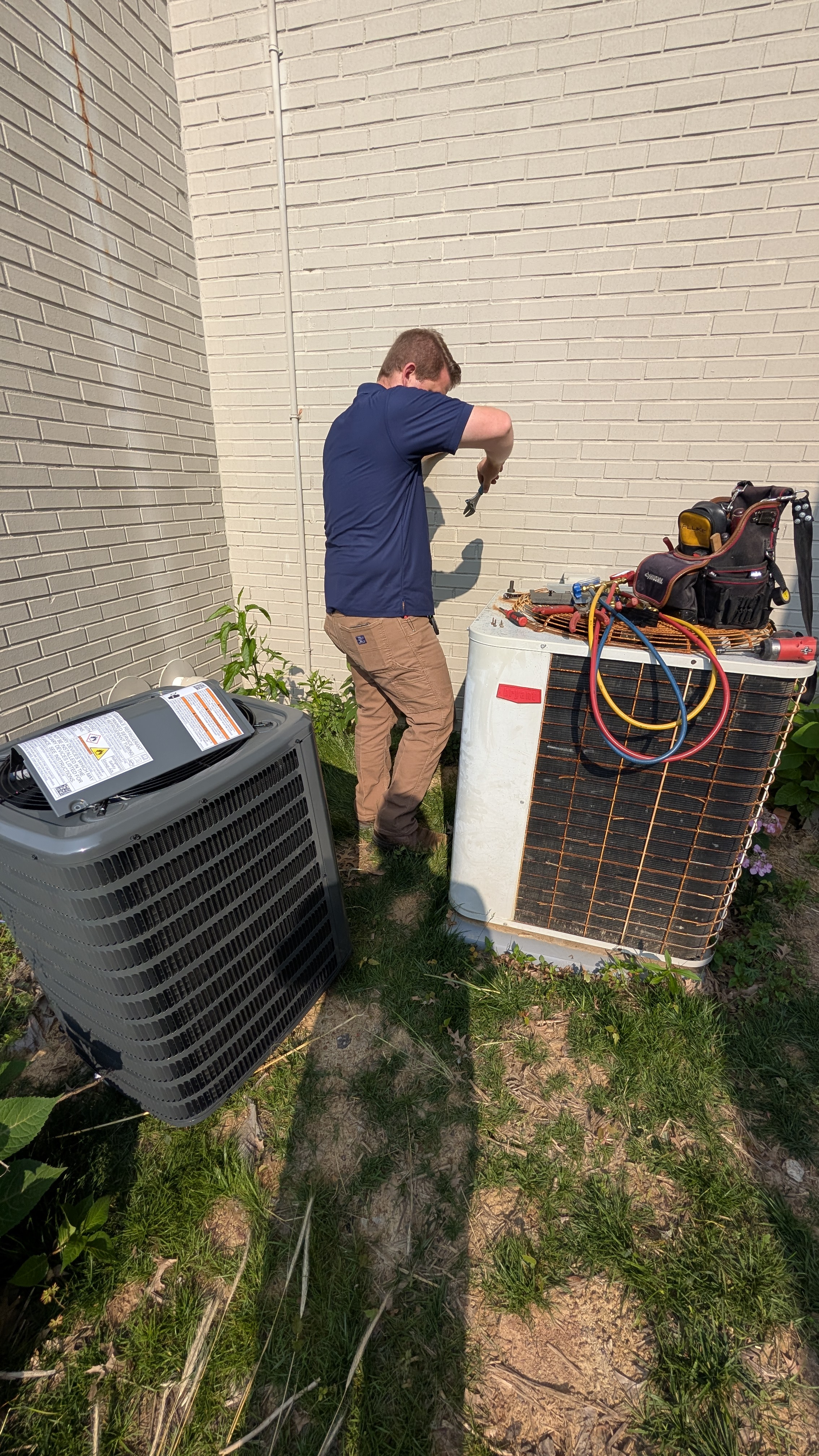 Two outdoor AC condenser units side by side with Henry Brothers technician working, New Albany Indiana