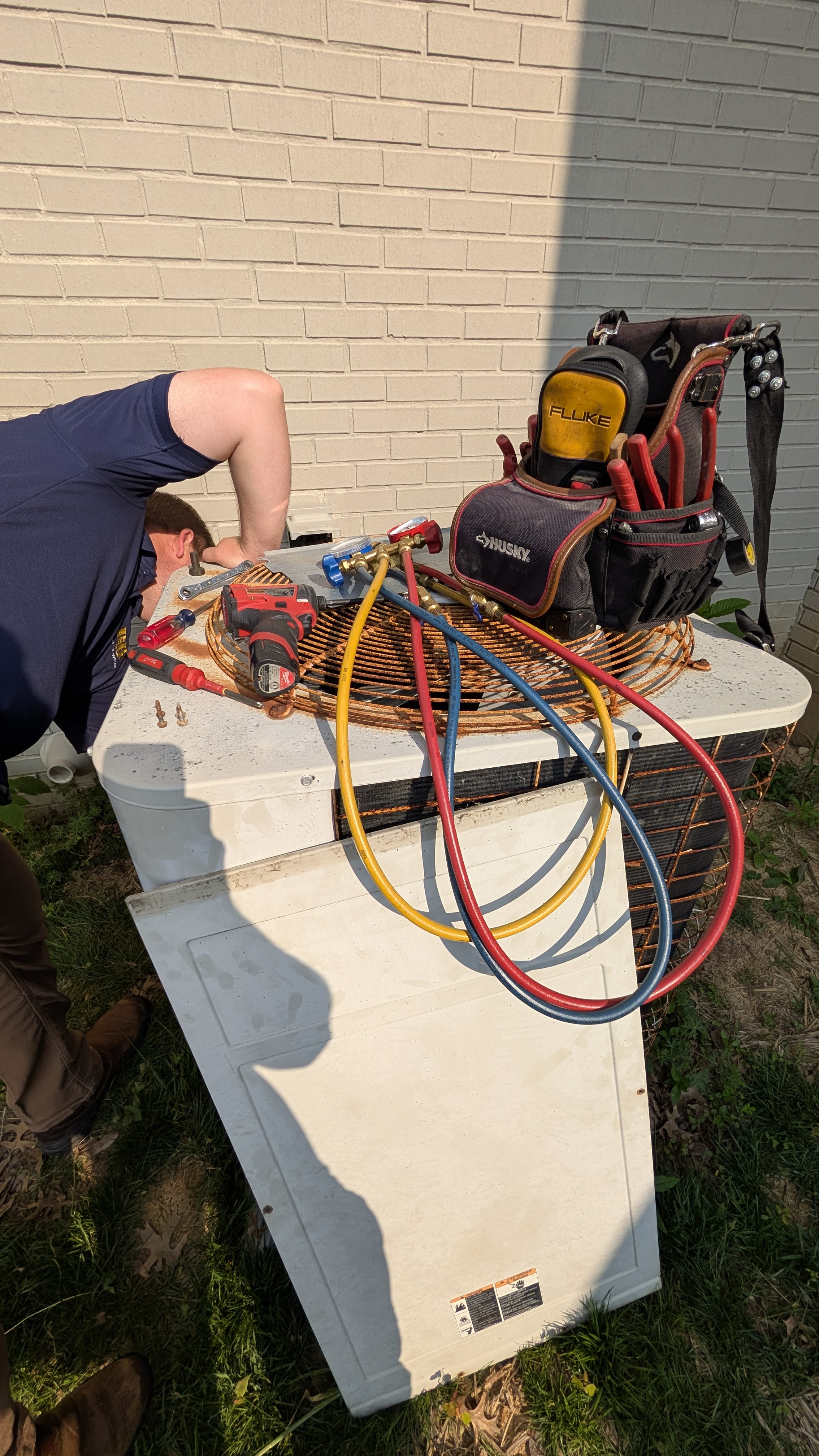 Henry Brothers technician servicing older central AC condenser unit with manifold gauges in New Albany Indiana