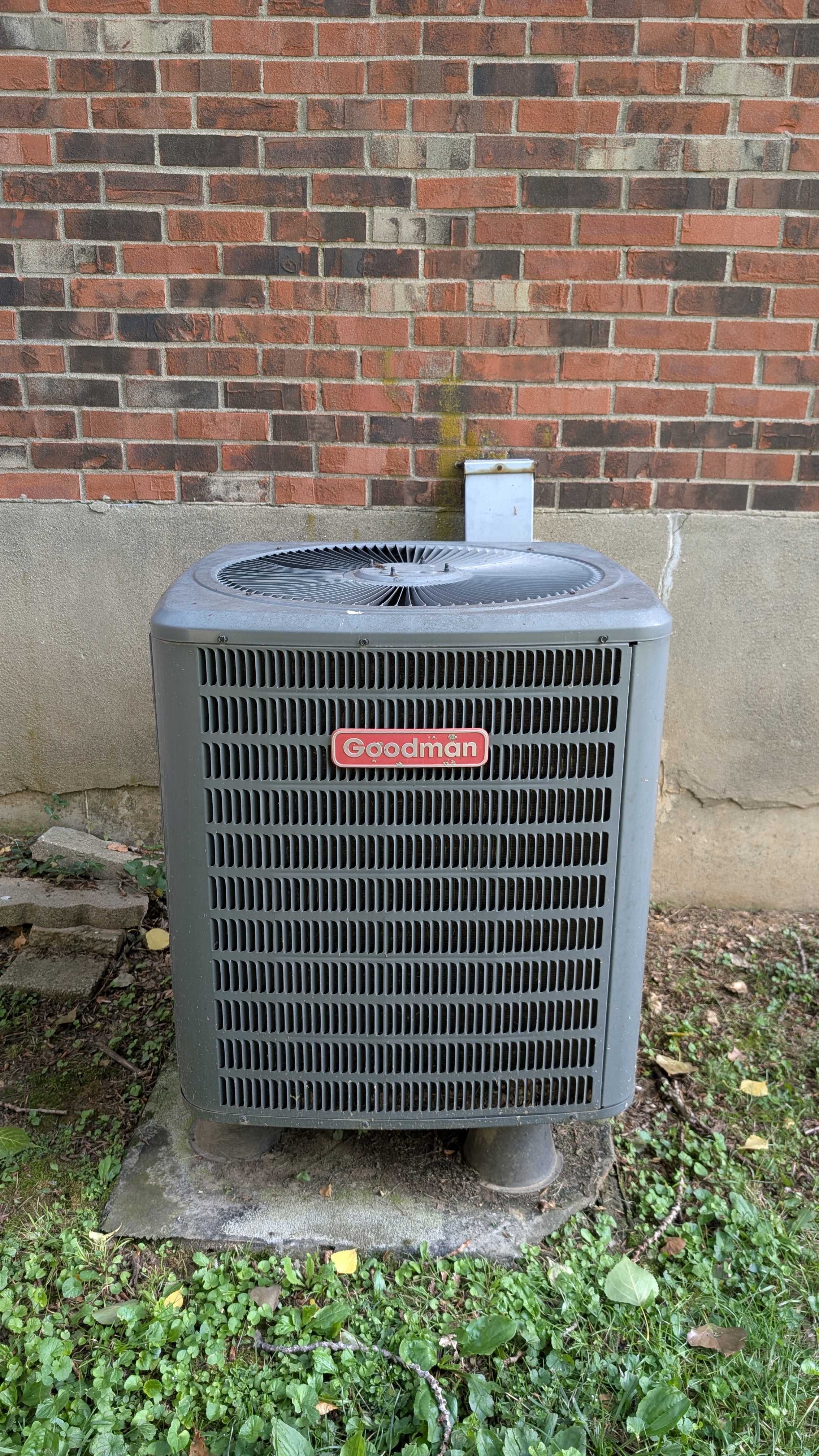 Goodman central AC condenser unit against brick wall before HVAC inspection