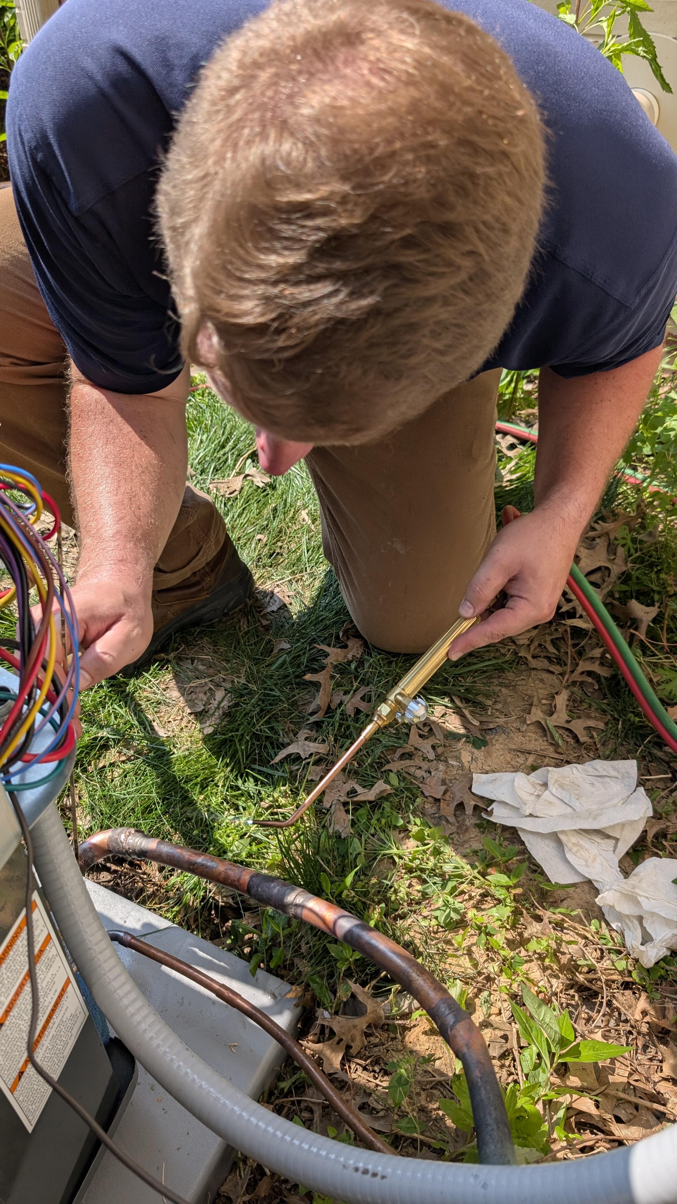 Close-up of HVAC technician brazing copper refrigerant line at outdoor condenser unit New Albany Indiana