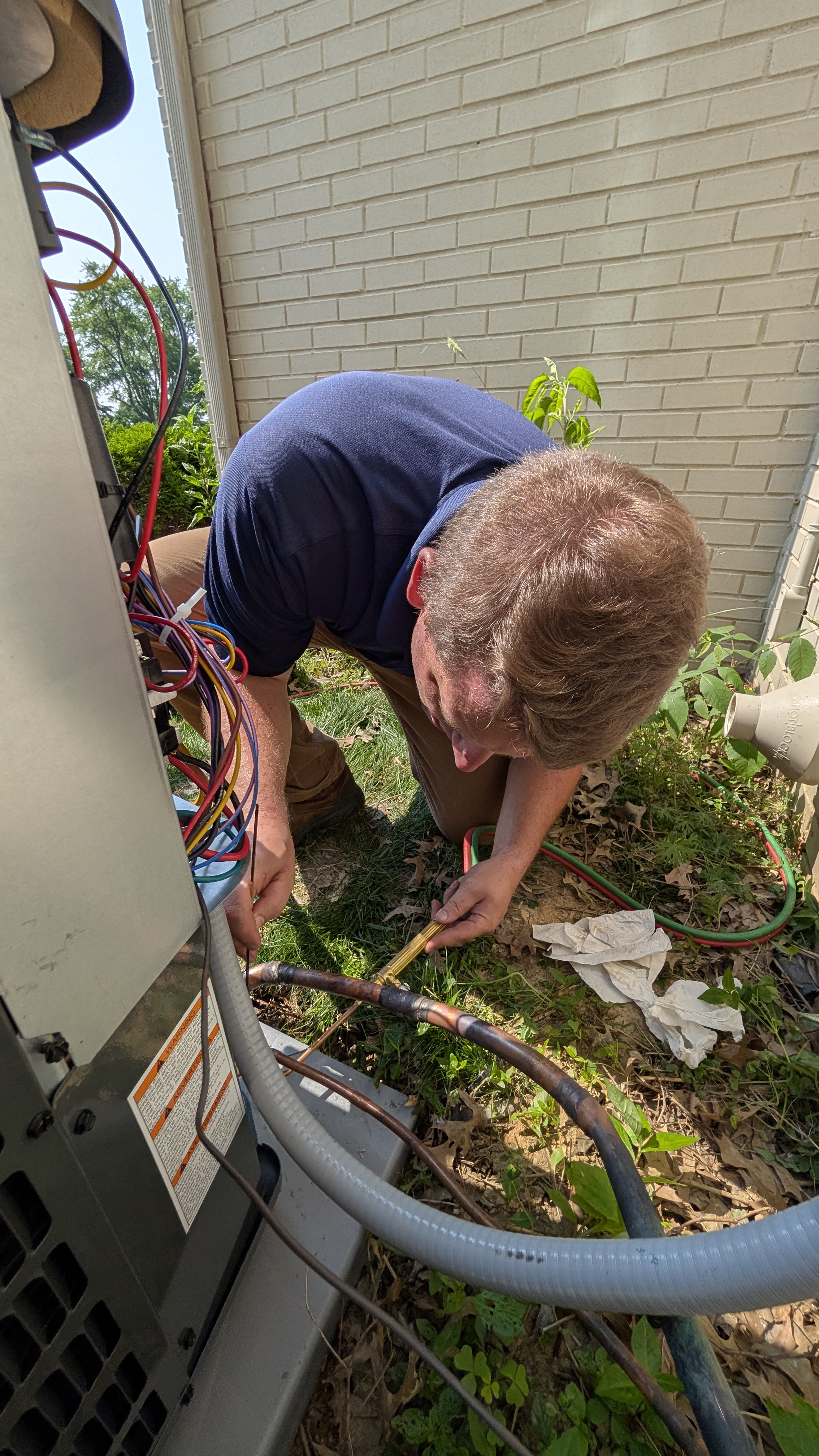 Technician soldering copper refrigerant lines at base of outdoor AC condenser in New Albany Indiana