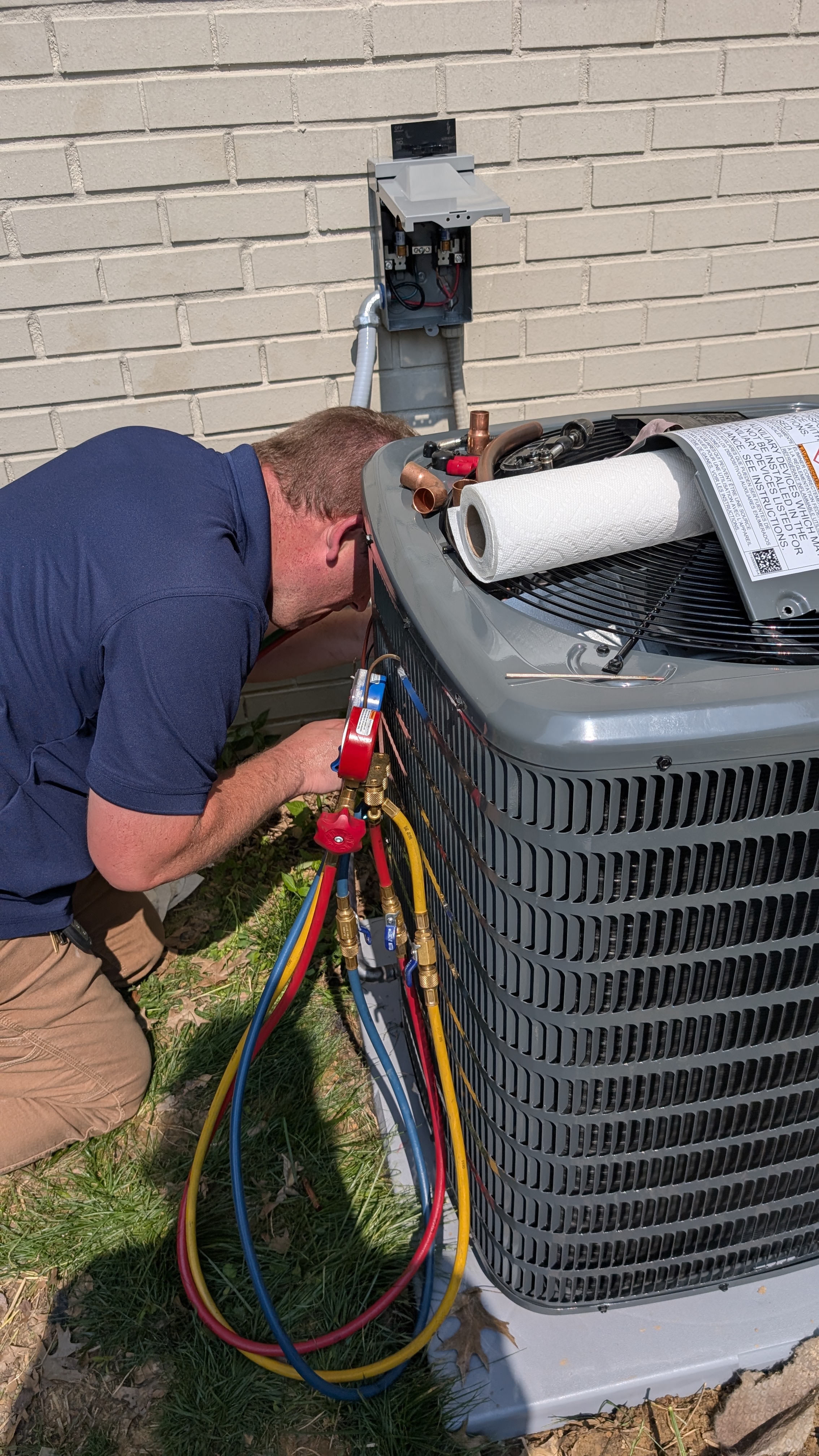 HVAC technician connecting manifold gauges to outdoor AC condenser unit in New Albany Indiana