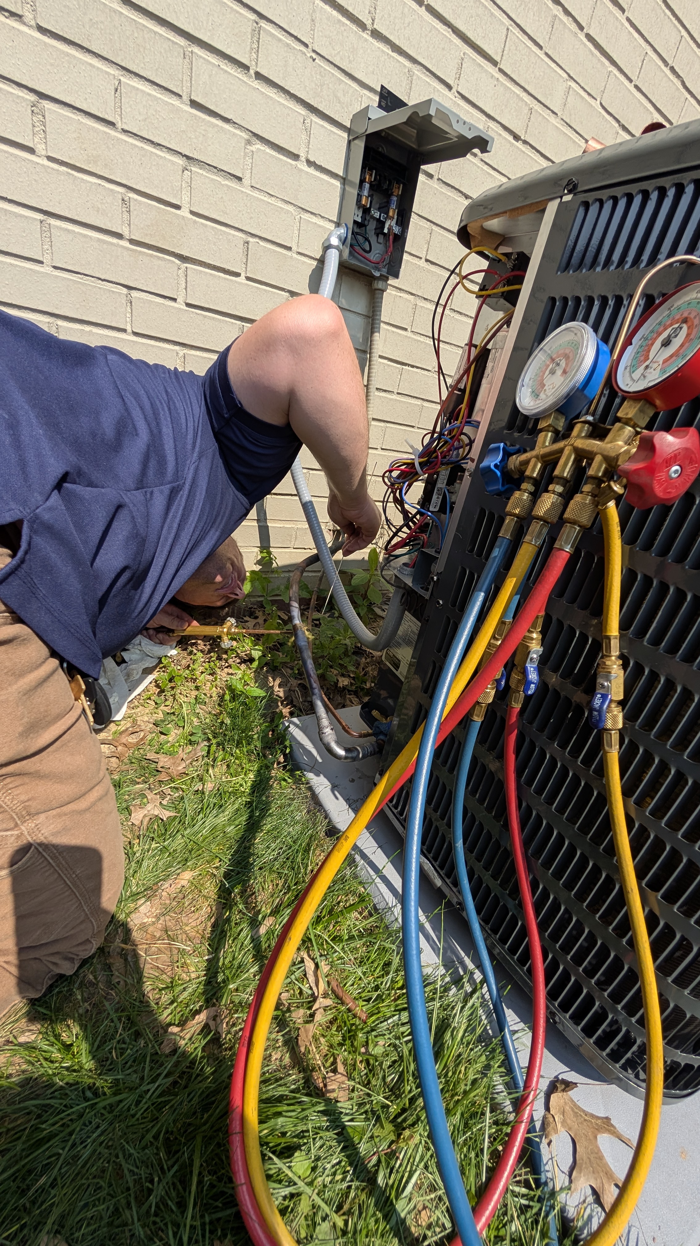Close-up of refrigerant manifold gauge set connected to AC condenser during HVAC repair in New Albany Indiana