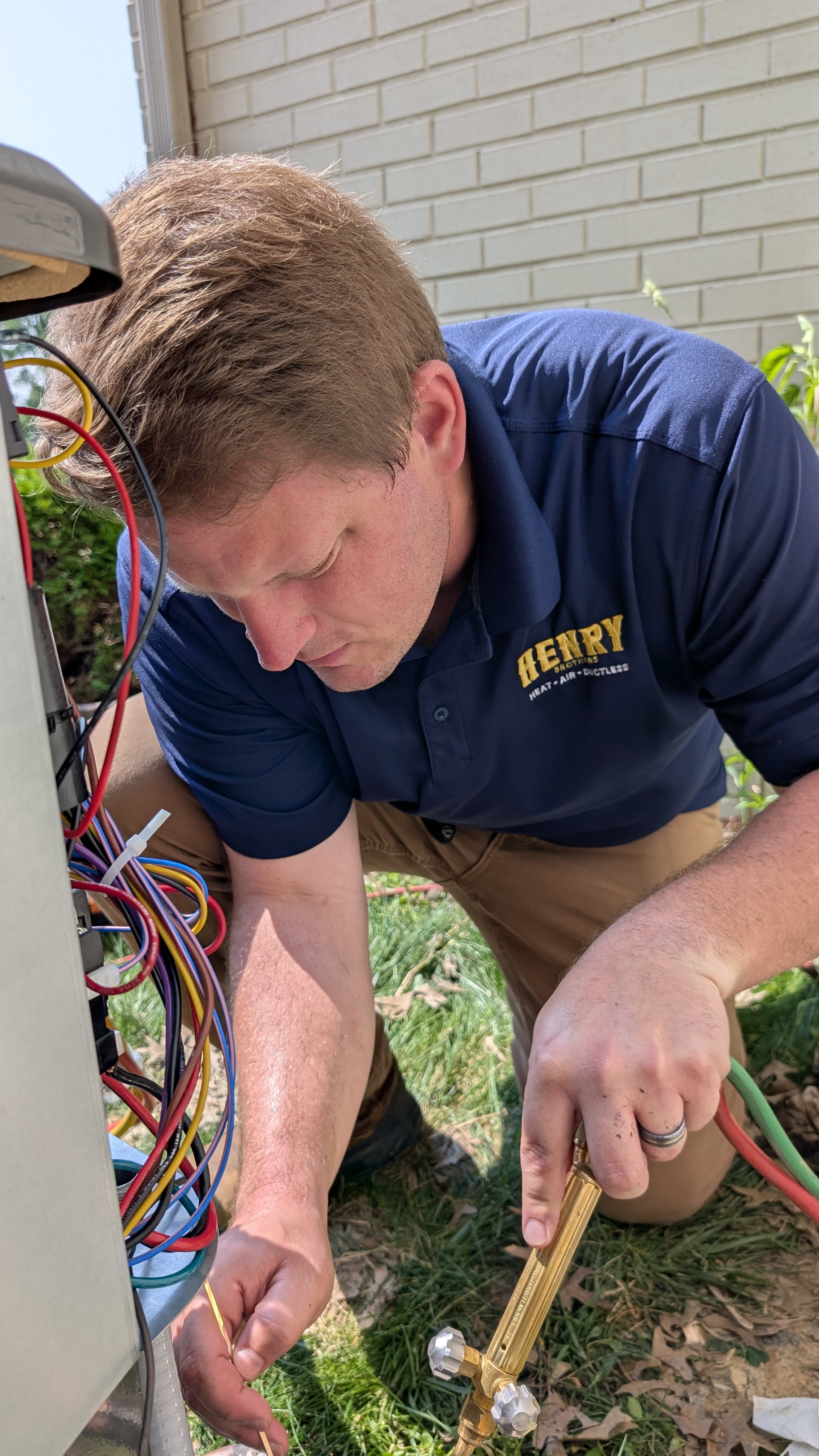 Henry Brothers branded technician brazing copper refrigerant line at outdoor AC condenser in New Albany Indiana
