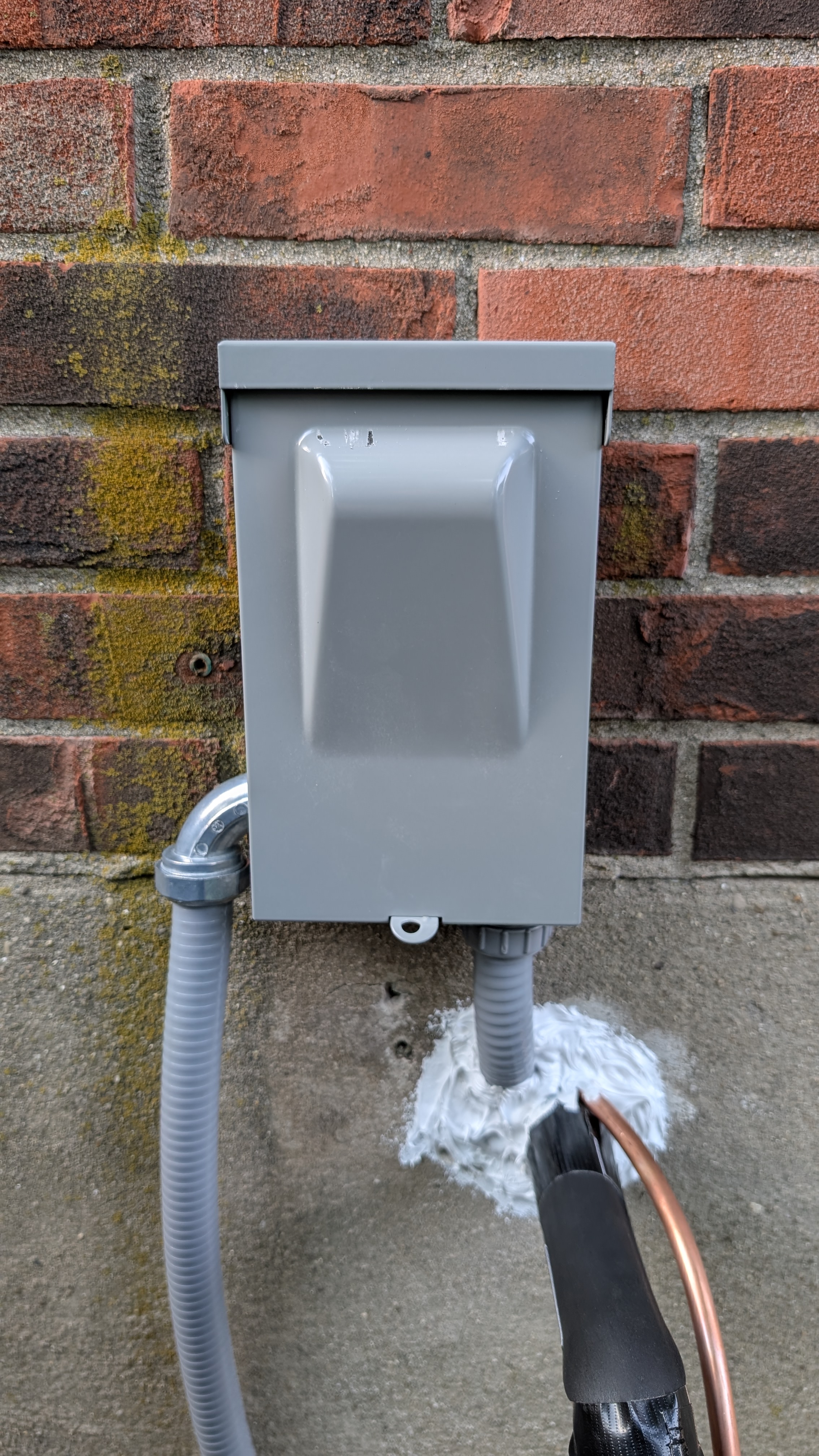 Newly installed outdoor AC disconnect box with conduit and copper line-set on brick exterior wall