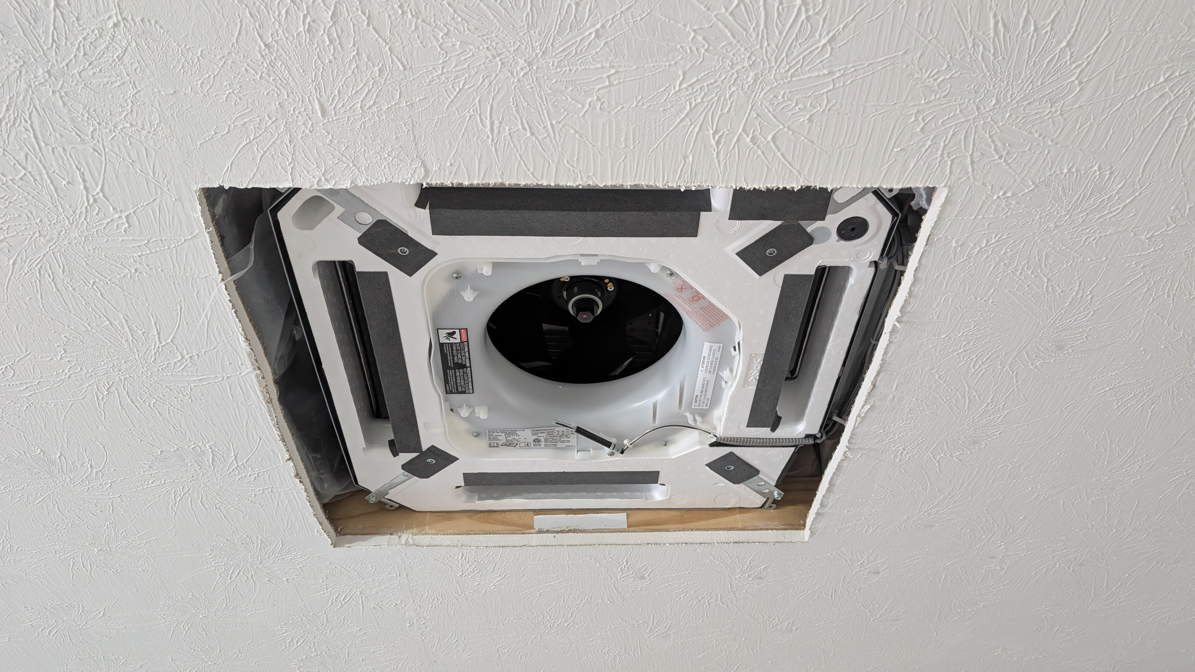 Ceiling cassette mini-split indoor unit with decorative panel removed showing internal fan and coil housing