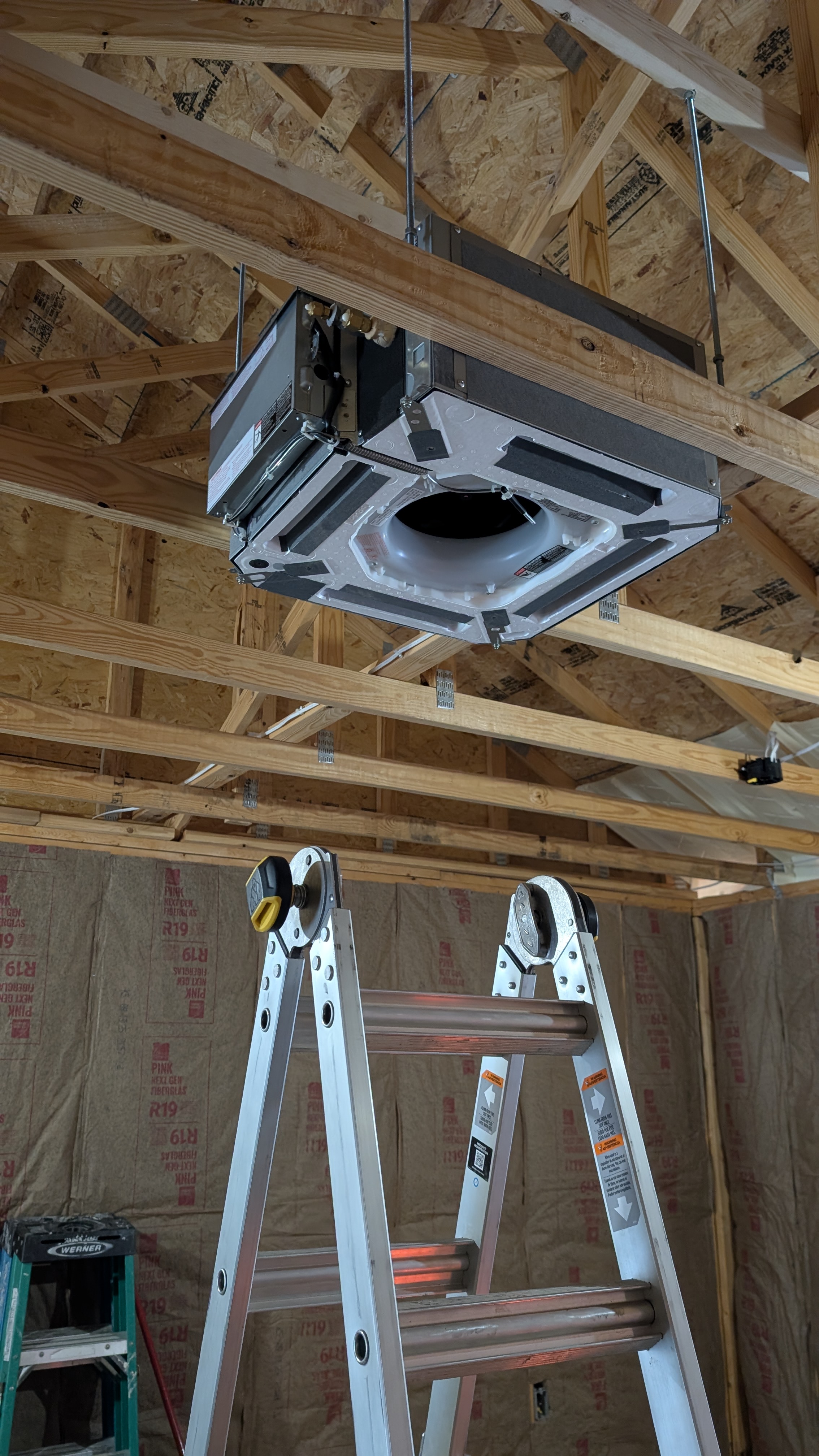 Ceiling cassette mini-split unit suspended in rough-framed outbuilding during installation