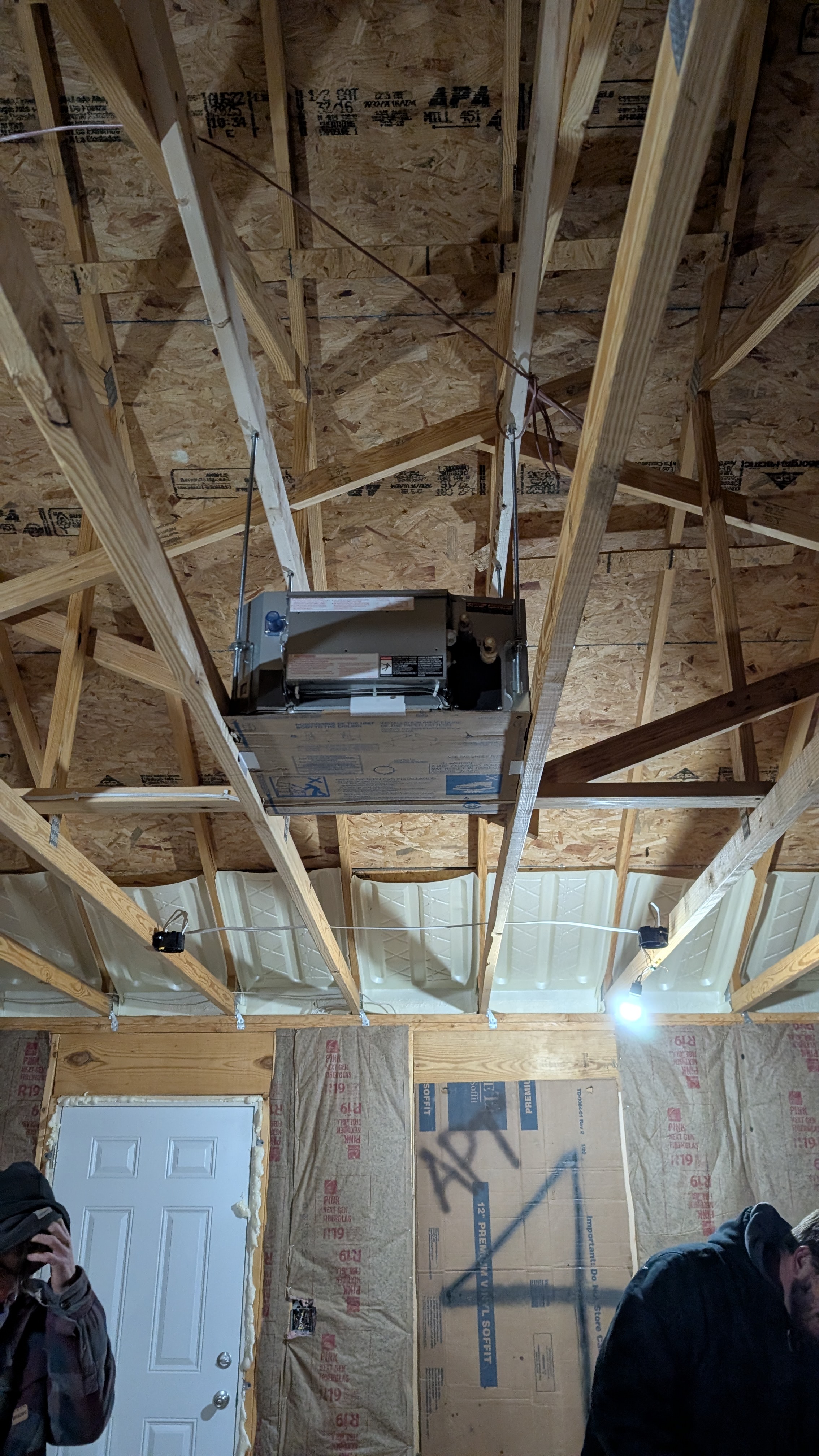 Technicians inspecting ceiling cassette mini-split unit in rough-framed new construction