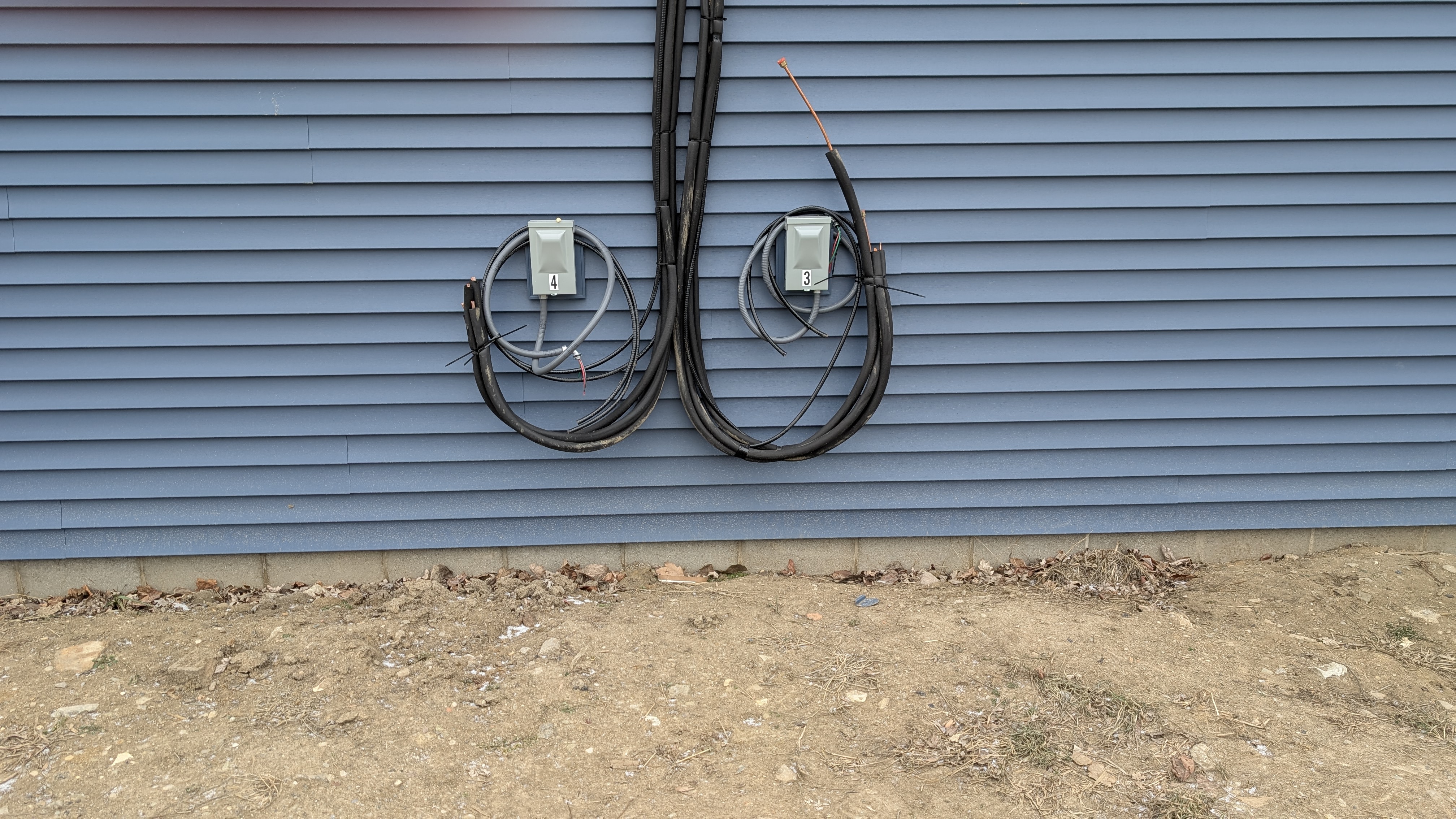Two sets of refrigerant line-sets and disconnect boxes staged on new-construction building exterior before condenser install