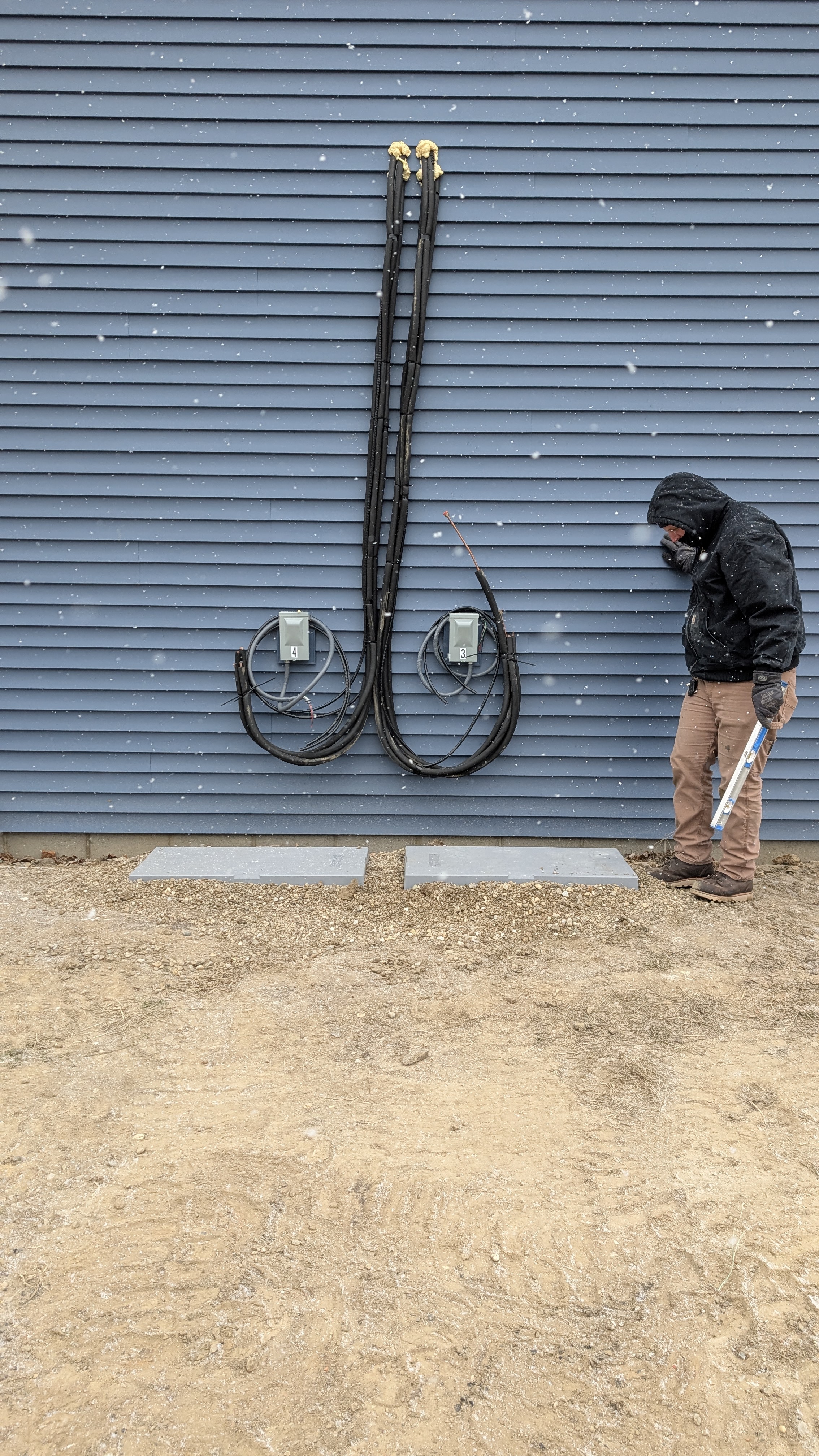 Technician working on dual-zone mini-split line-set and disconnect boxes on building wall in snow