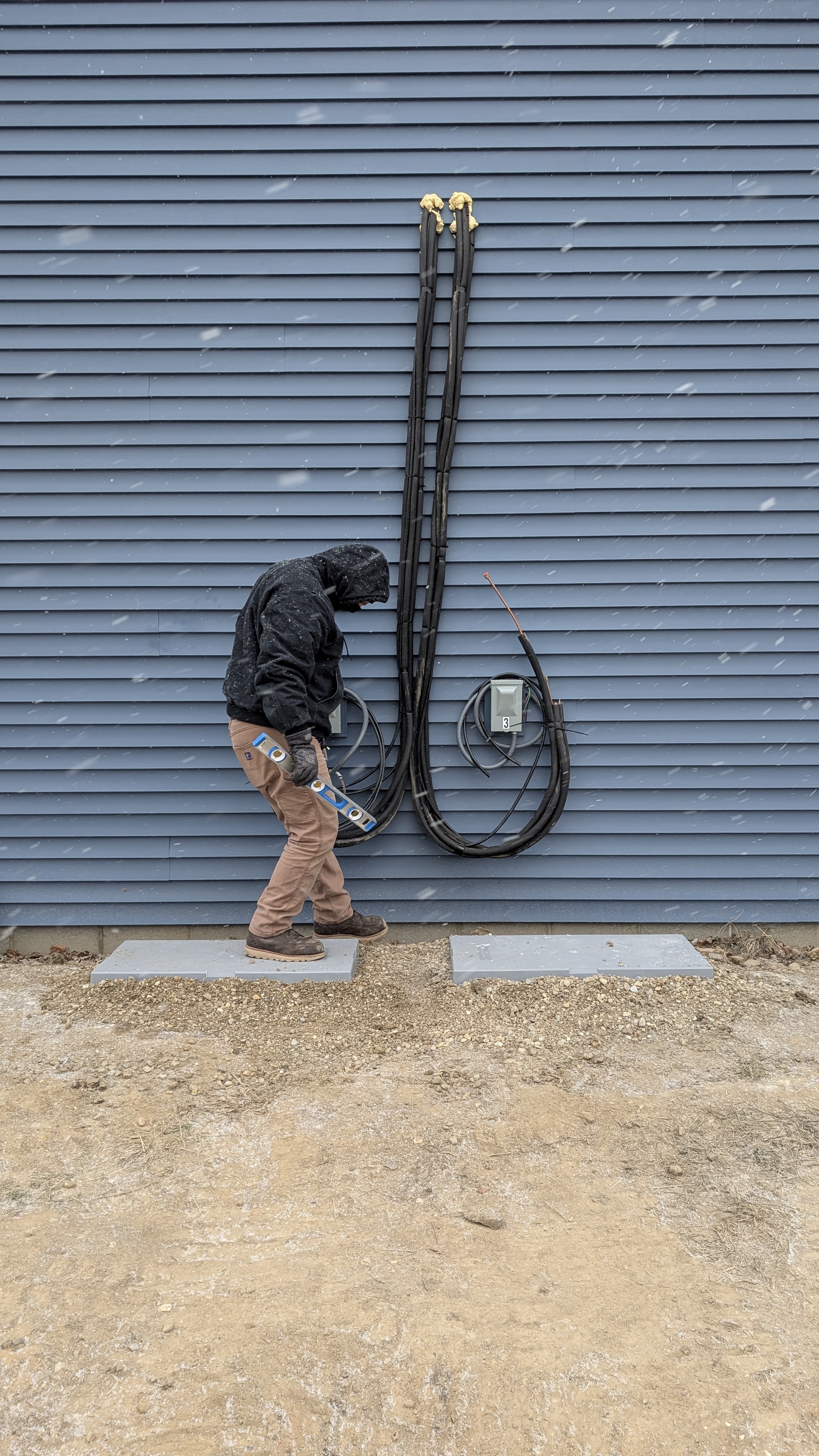 Technician routing line-set for dual-zone Daikin mini-split install on new-construction exterior in snow