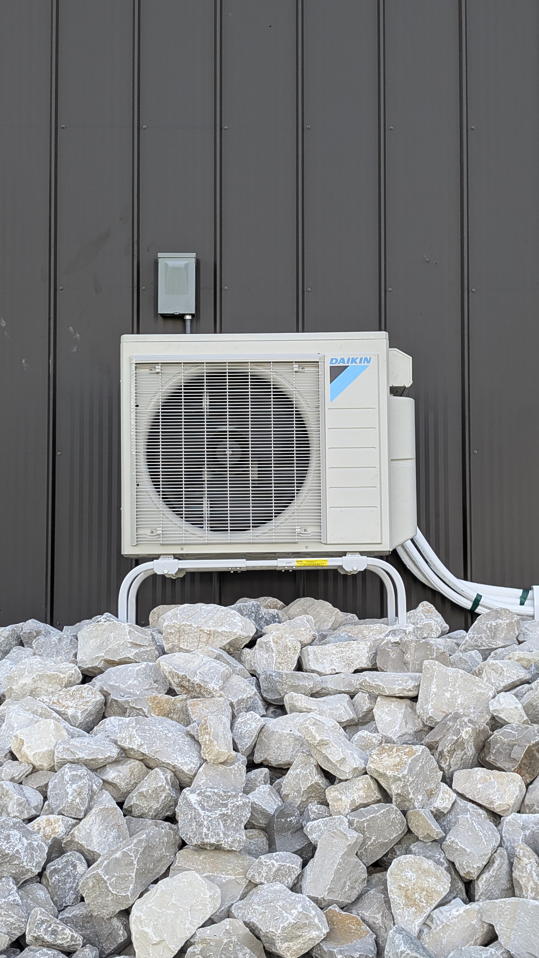 Completed Daikin mini-split outdoor condenser unit mounted on brackets beside dark metal barn Indiana