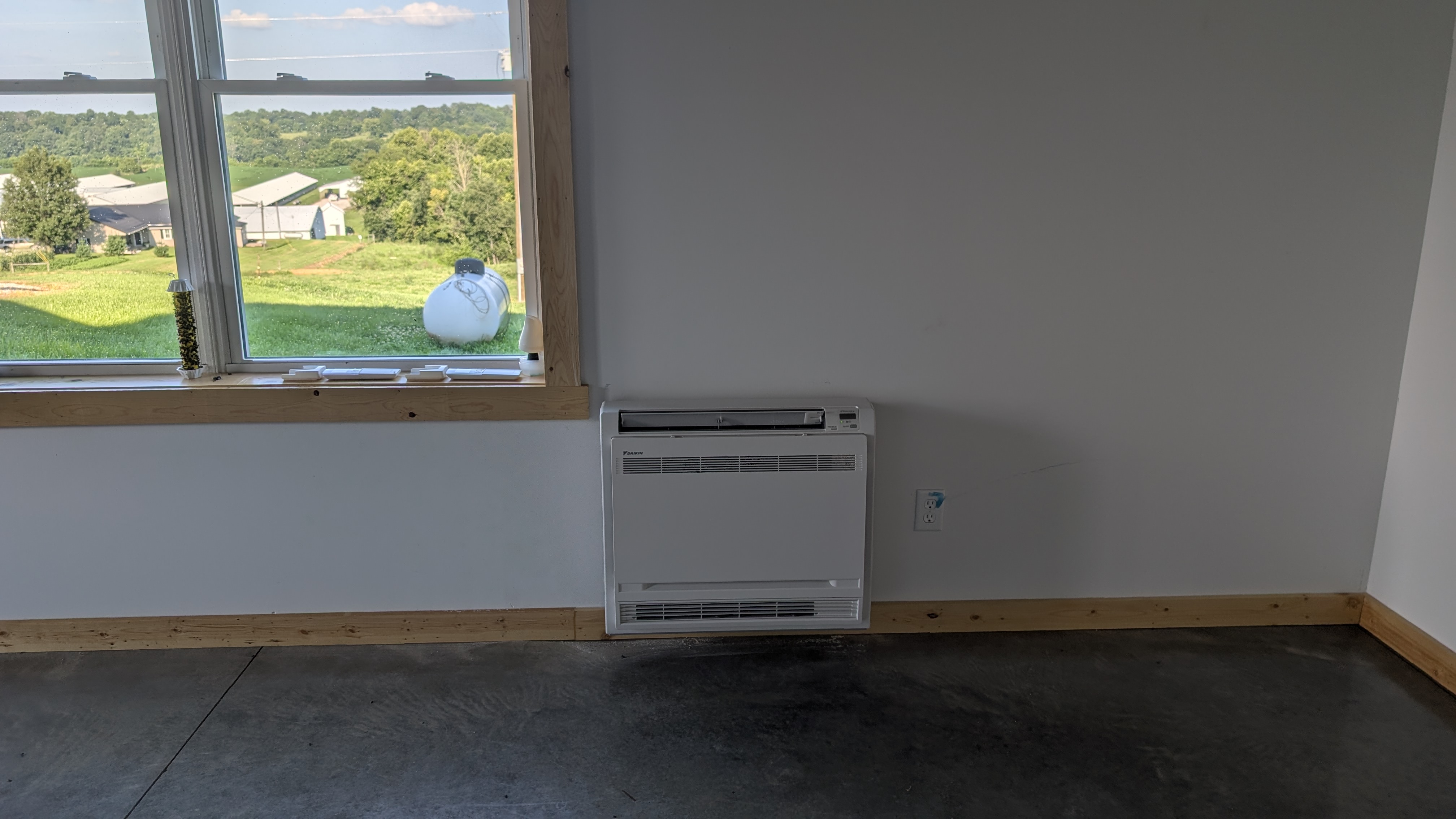 Completed Daikin floor-console mini-split install inside pole barn with sunny Indiana farmland through window