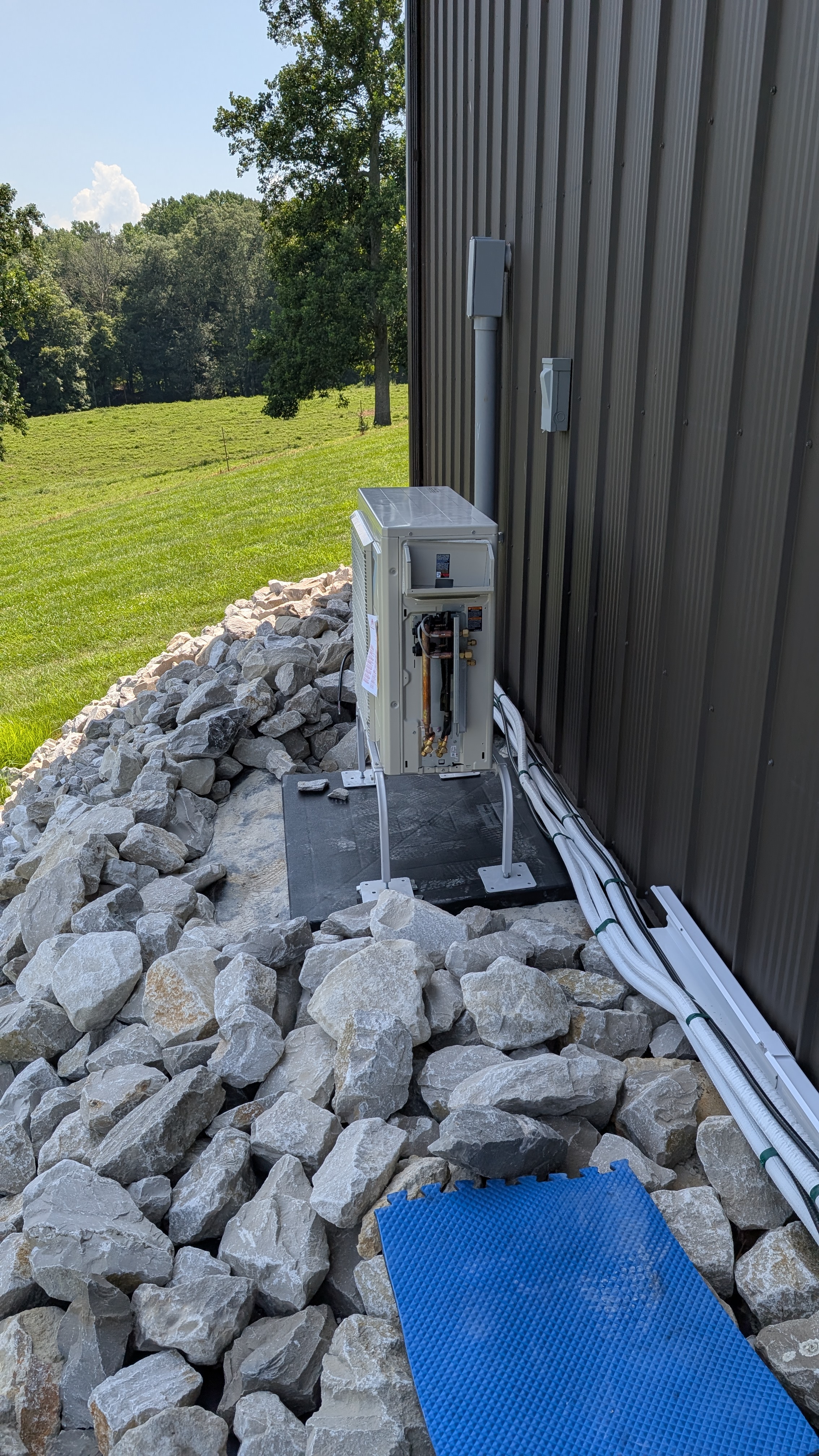 Daikin mini-split condenser mid-install on rock bed beside dark metal pole barn Indiana