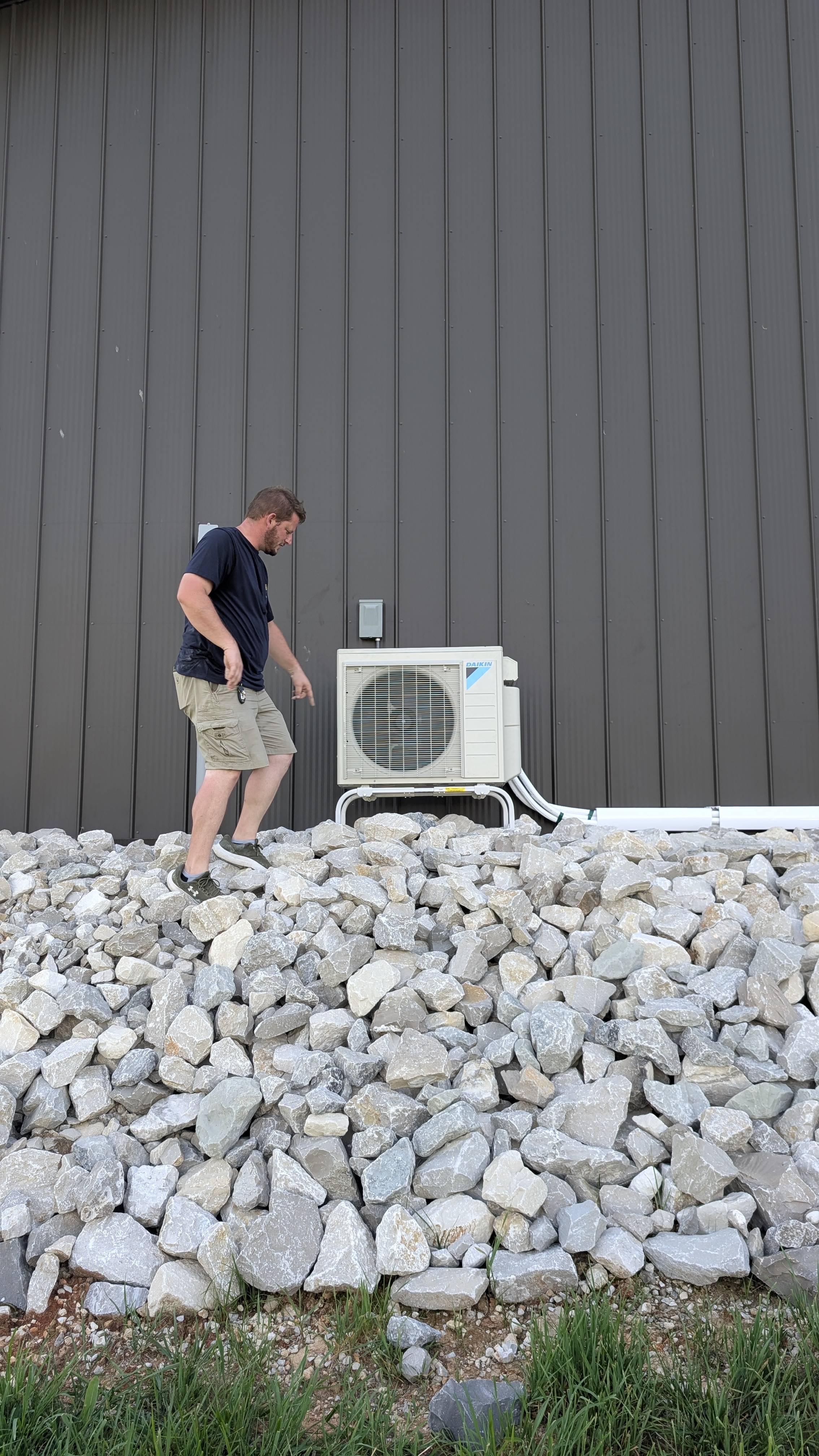 Henry Brothers HVAC technician on rock bed next to installed Daikin outdoor condenser unit
