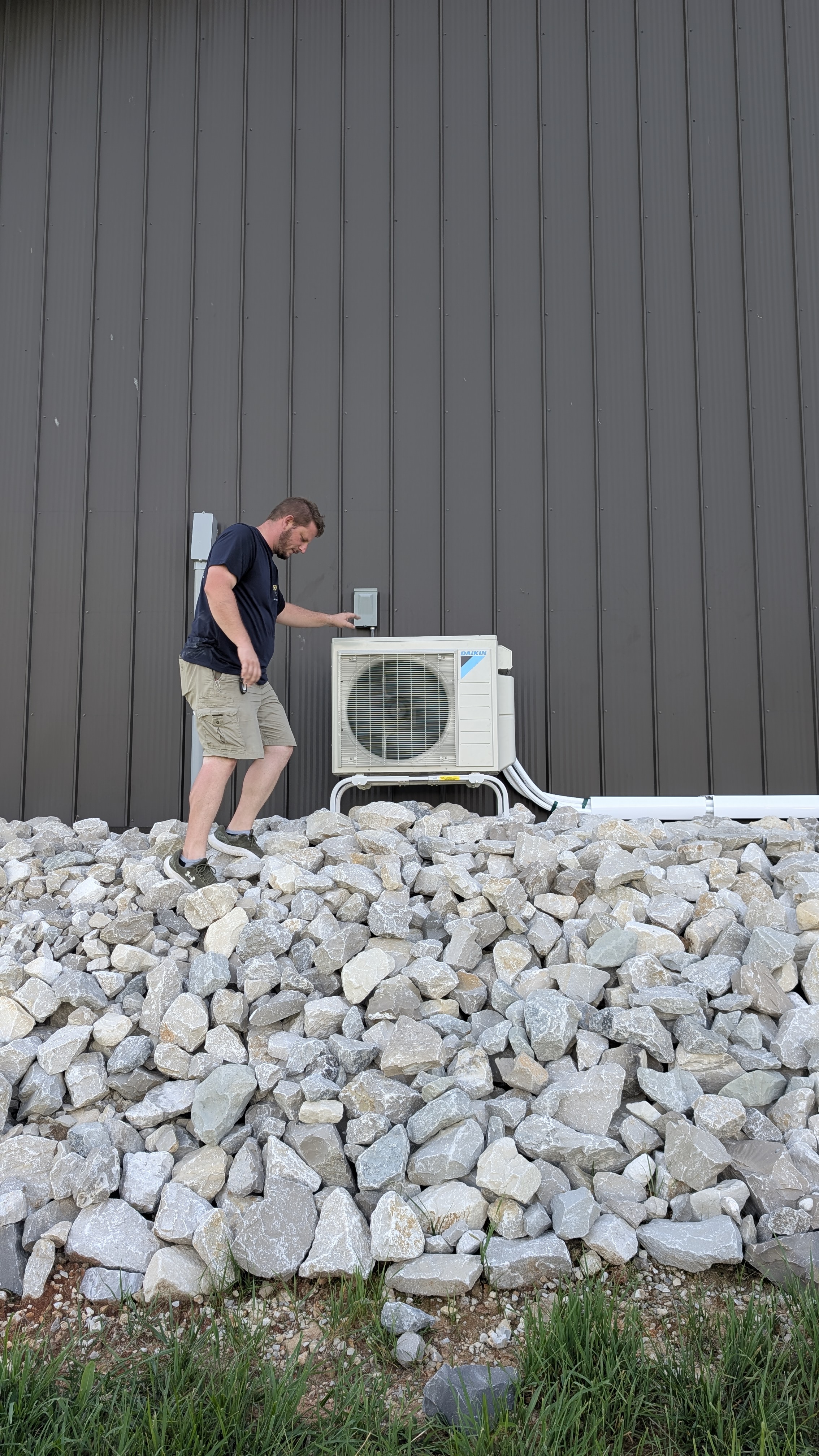 Technician beside completed Daikin mini-split outdoor unit mounted on pole barn wall Indiana
