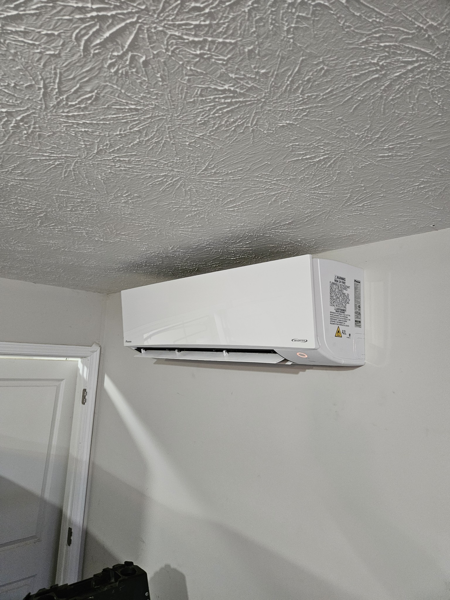 Daikin Inverter ductless indoor unit mounted high on wall near doorway with popcorn ceiling