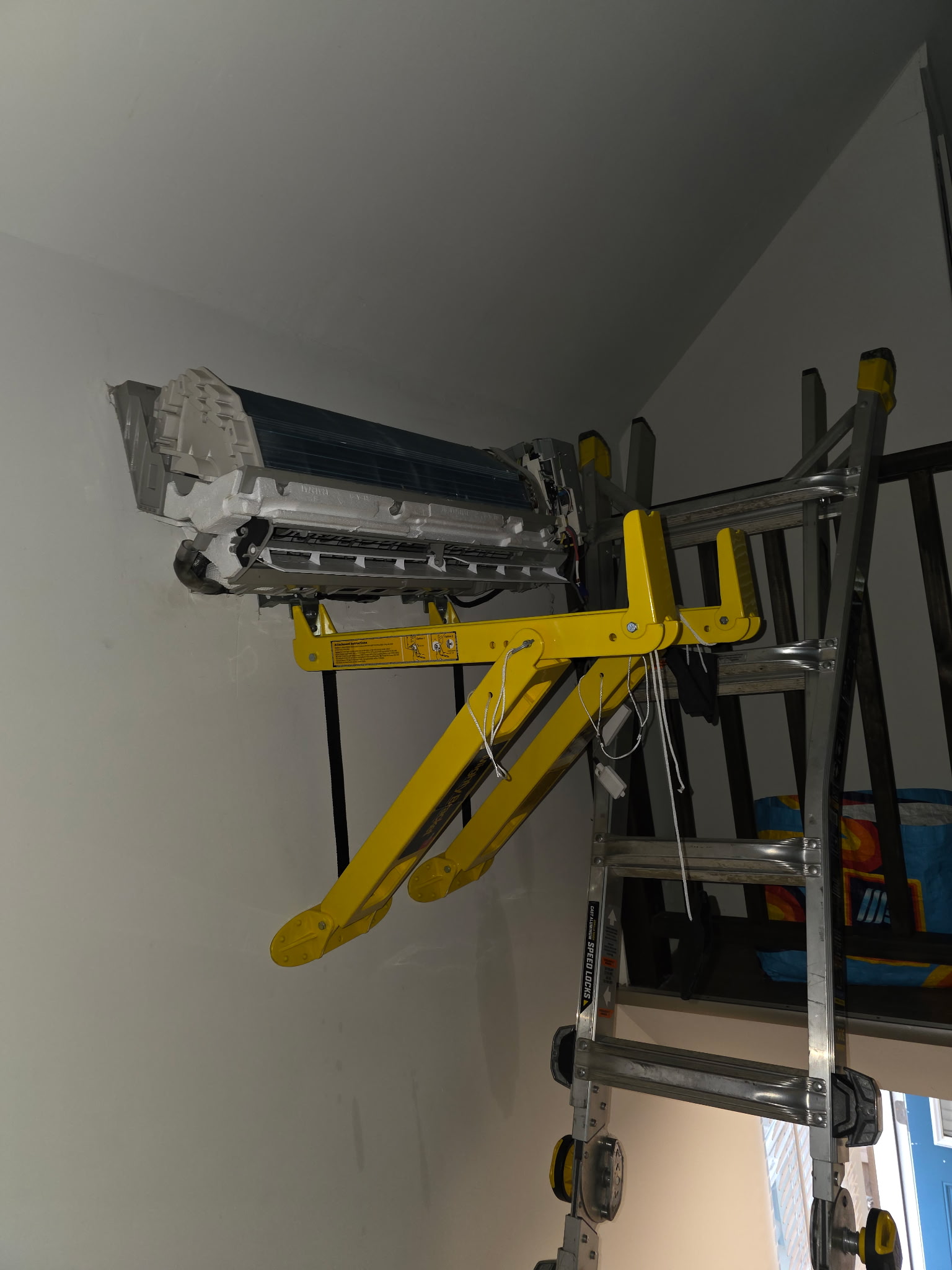Mini-split indoor head unit suspended on wall lift bracket during high-wall installation process