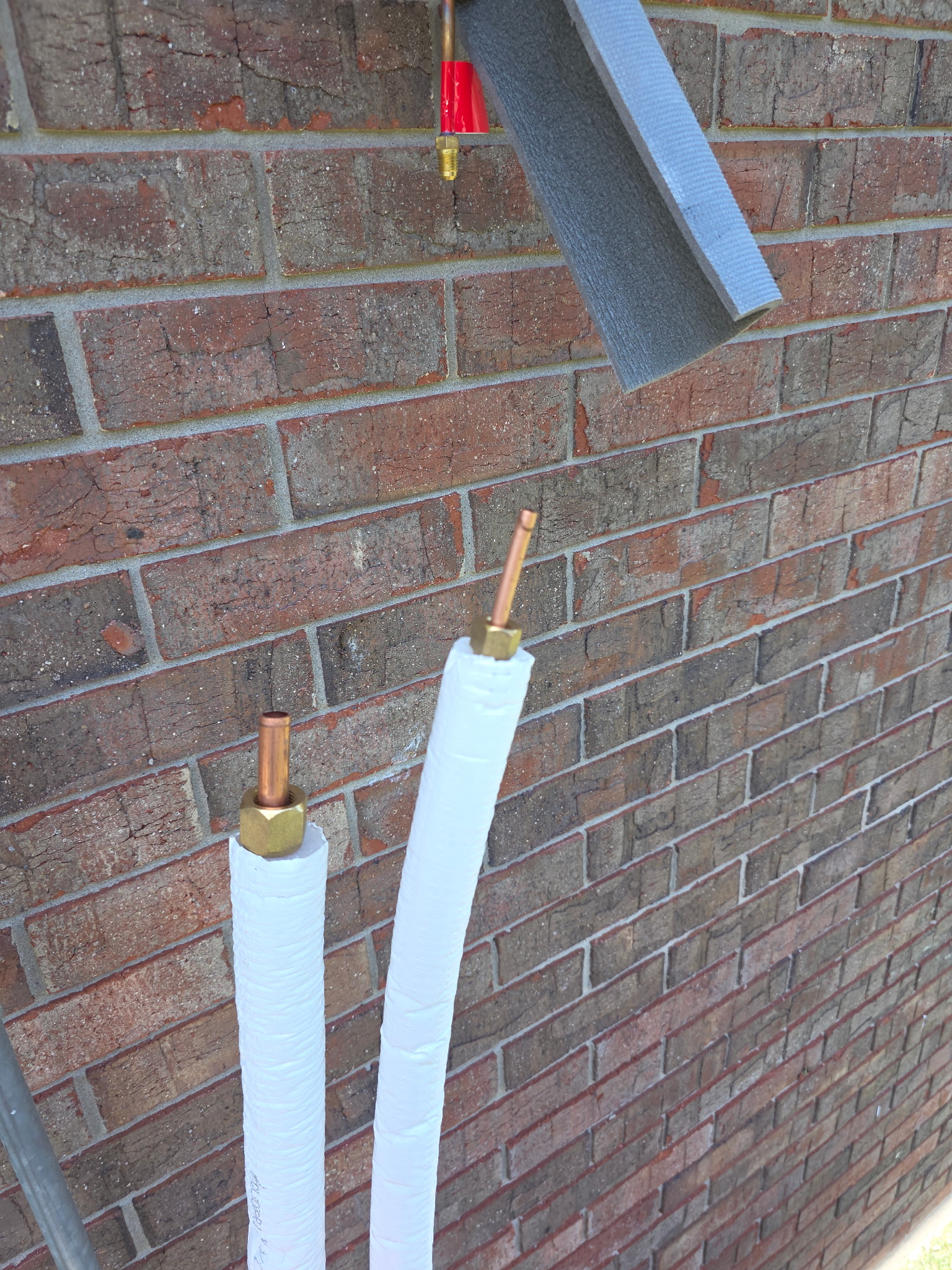 Insulated copper refrigerant line set pipes staged against brick wall before mini-split connection