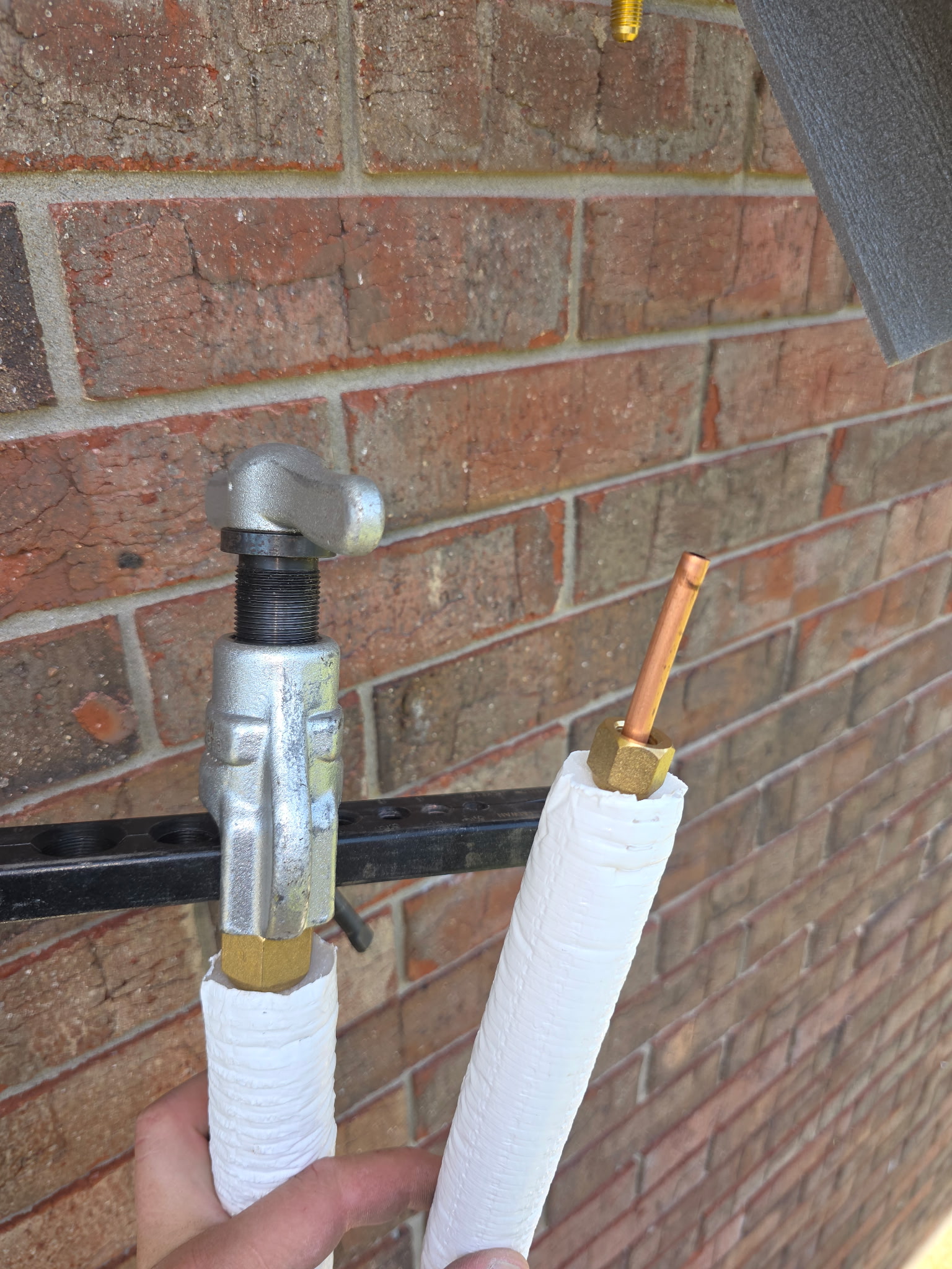 Close-up of mini-split refrigerant line set flare fittings being connected at brick wall