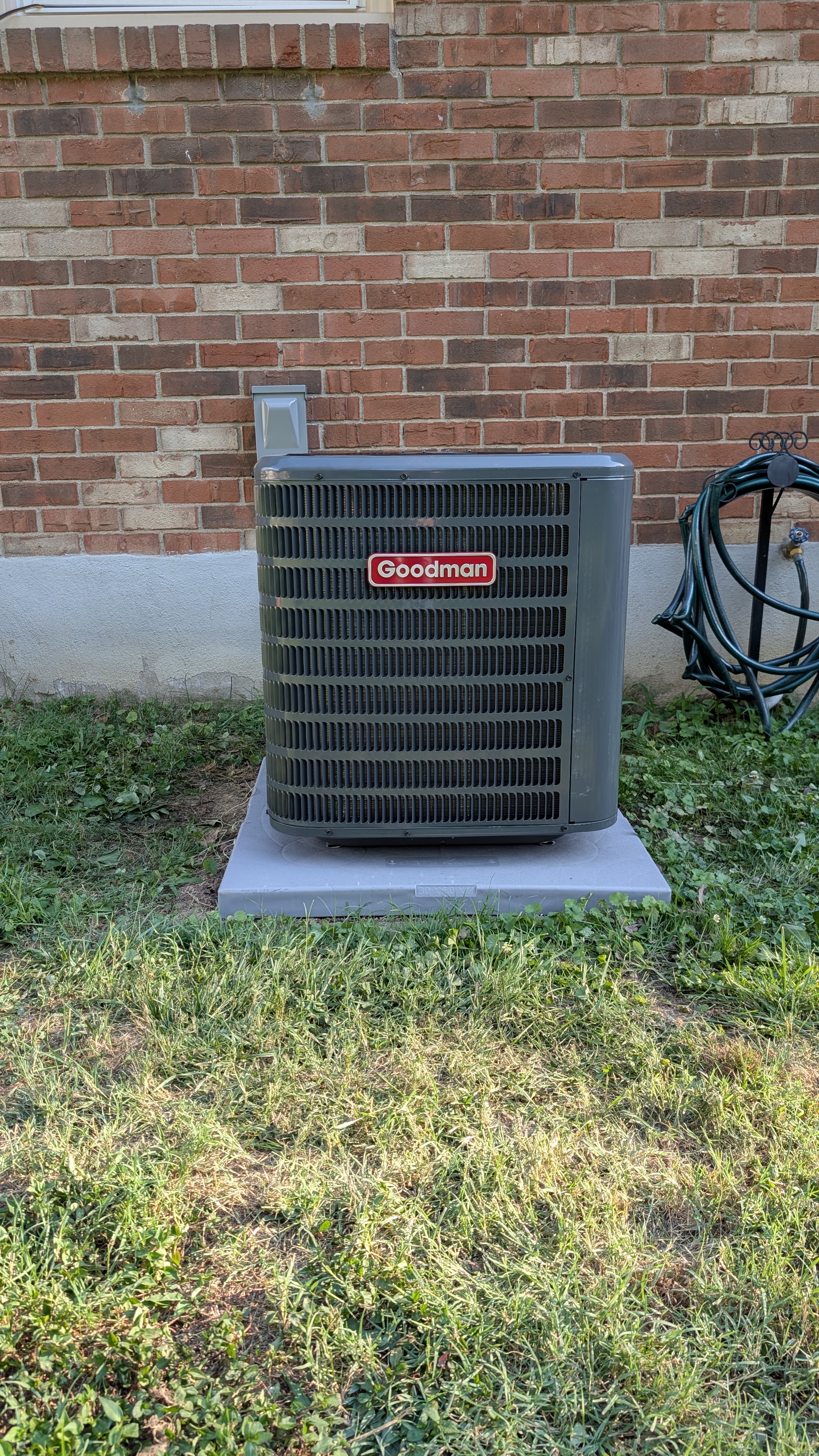 Goodman AC condenser on concrete pad beside brick home wider view